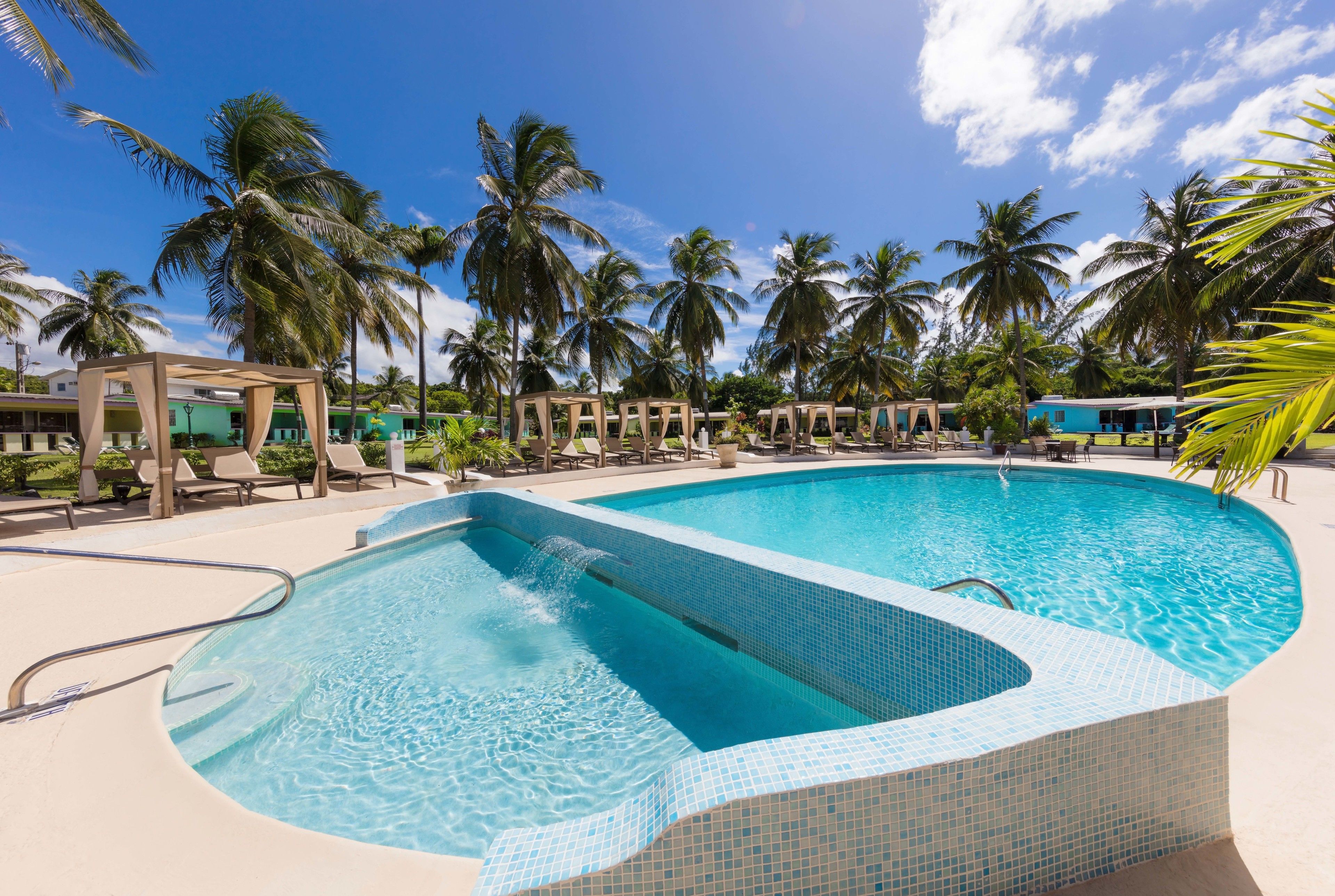 Una piscina con bordes de azulejos, rodeada de sillas de descanso y palmeras.