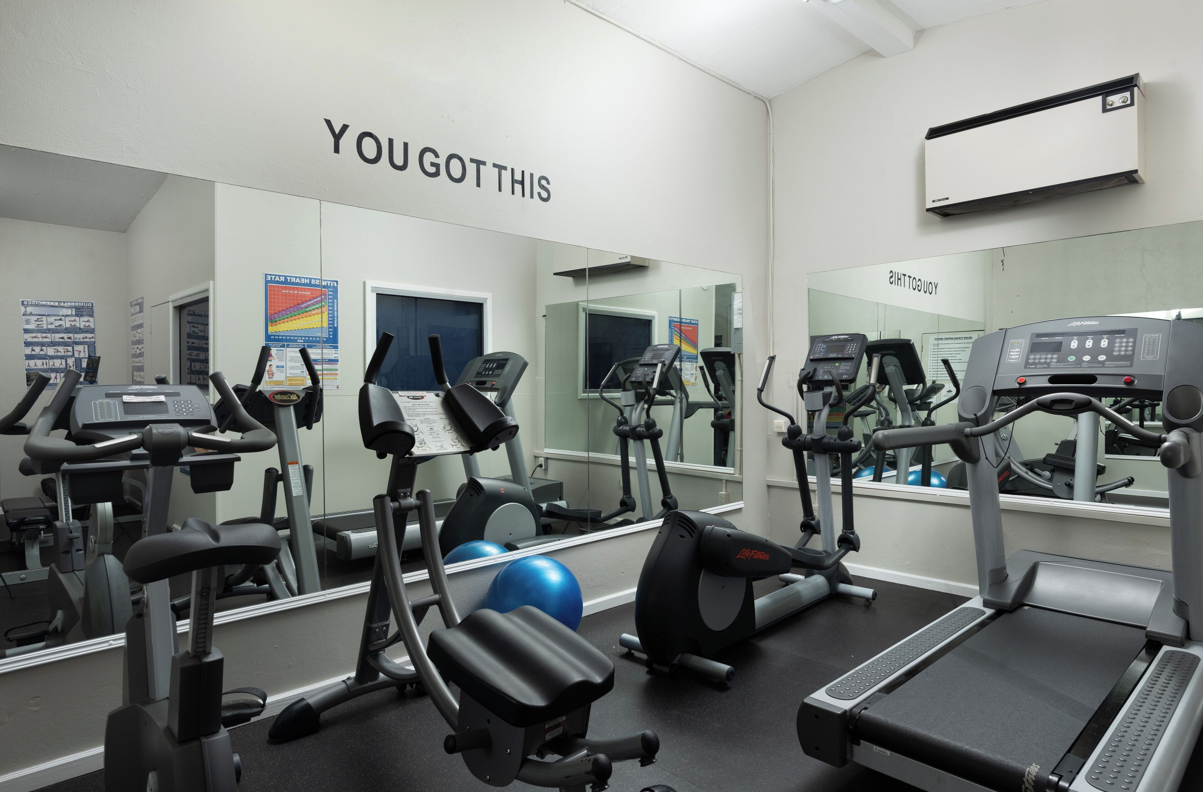 A gym with various exercise equipment, a blue exercise ball, and motivational posters on the walls.