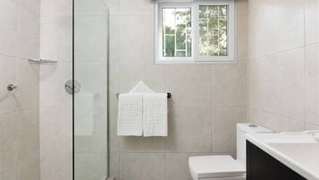 Een badkamer met een douchecabine van glas, een toilet en een raam boven de wastafel.