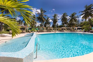 A clear blue pool surrounded by lounge chairs and palm trees, with a tiled edge and a metal ladder. - All Seasons Resort - Europa (Holetown)