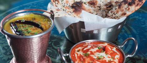 A meal with naan bread, a bowl of curry, and a cup of sauce.