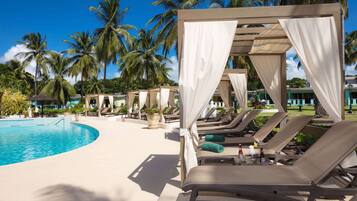 A resort pool area with sun loungers, a pool, and palm trees.