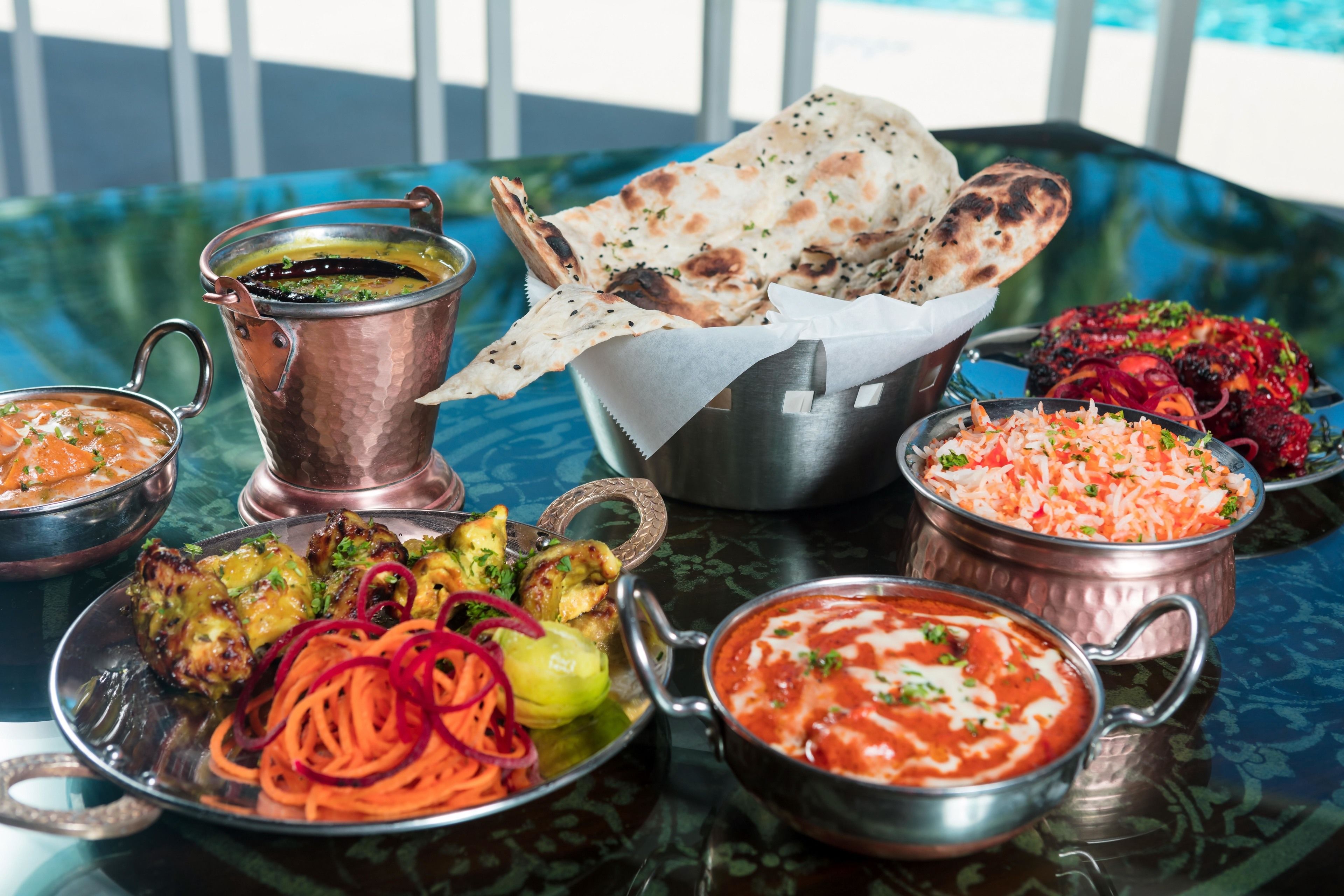 Un tavolo con diversi piatti indiani, tra cui una pentola di rame, una ciotola di curry e pane naan.