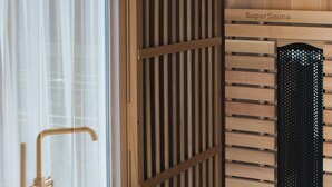 Uma sauna com ripas de madeira e porta de vidro, um banco de madeira e uma placa com a inscrição 'SuperSauna'.