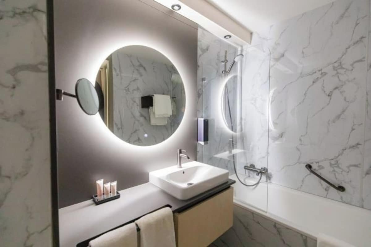 A modern bathroom with a round mirror, a white sink, and a glass-enclosed shower.