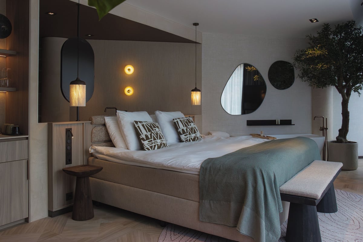 A modern bedroom with a bed, bedside tables, a mirror, and a potted plant.