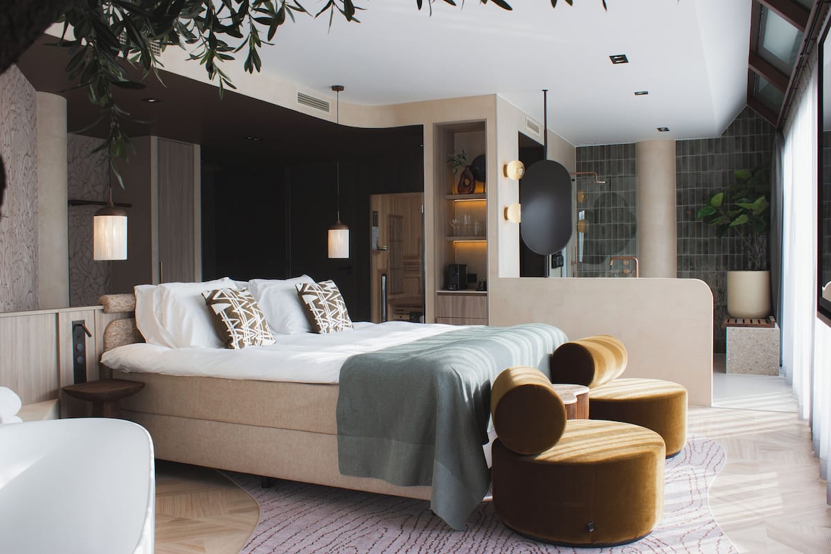 A modern bedroom with a large bed, bedside tables, a seating area with ottomans, and a built-in wardrobe.