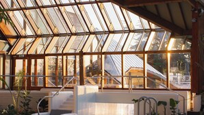 Piscina interior com teto de vidro, rodeada por plantas e uma escadaria que dá acesso a níveis superiores.