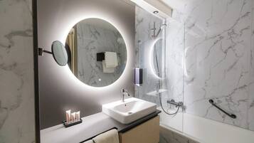 Een moderne badkamer met een marmeren wand, een ronde spiegel, een wit wastafelmeubel en een douche met glazen wanden.