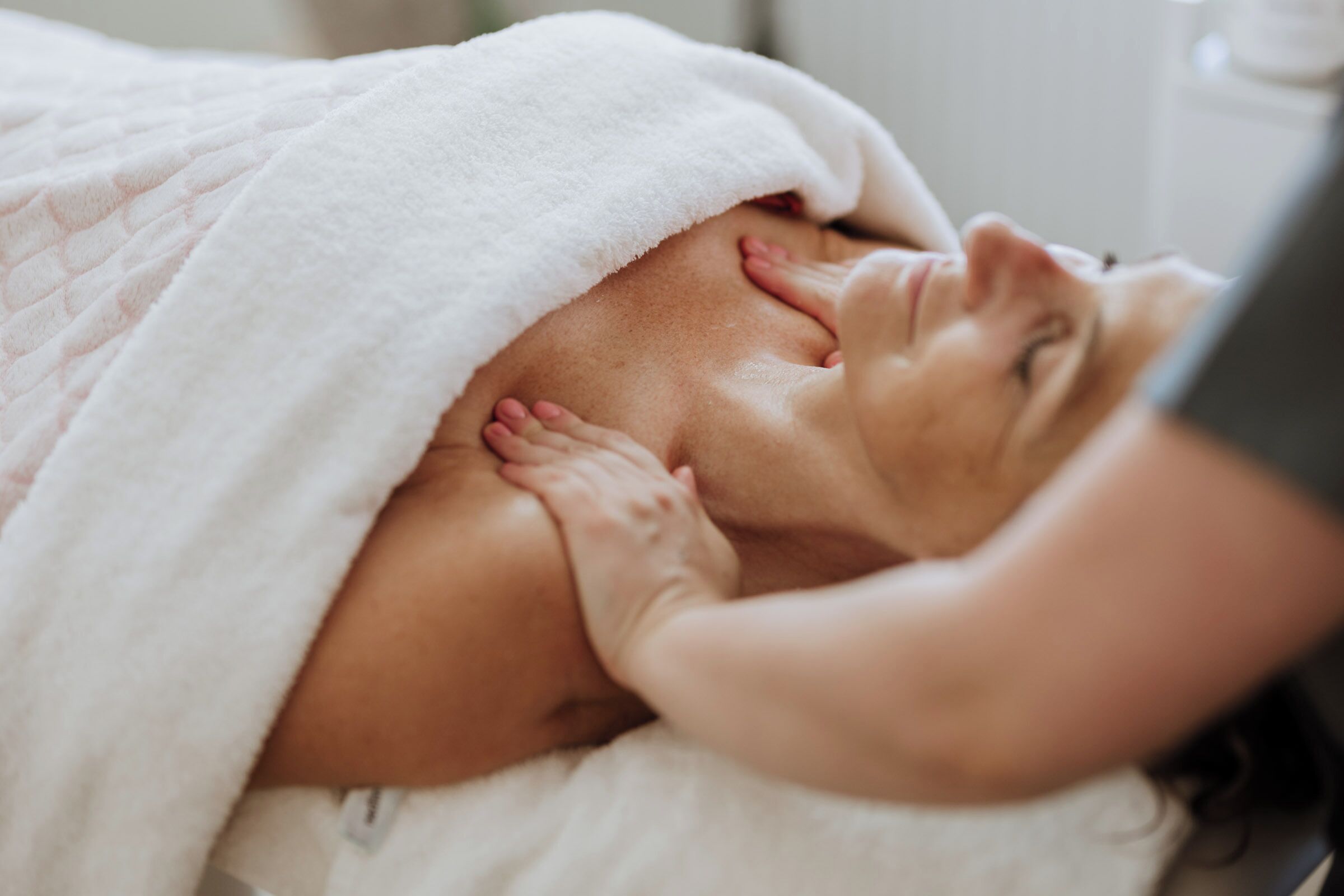Eine Person liegt entspannt mit einem weißen Handtuch, das den Kopf bedeckt, was an ein Wellness- oder Entspannungsambiente erinnert.