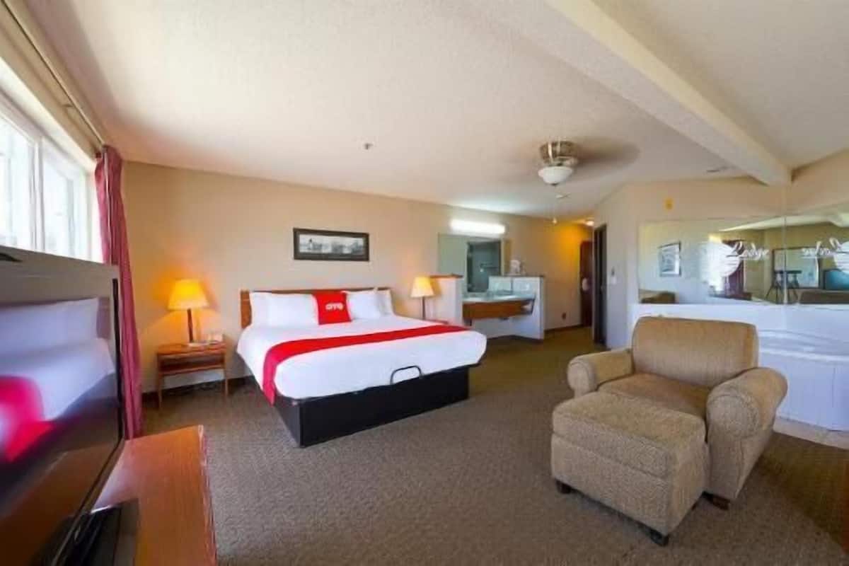 A hotel room with a bed, a chair, a desk, a mirror, and a window.