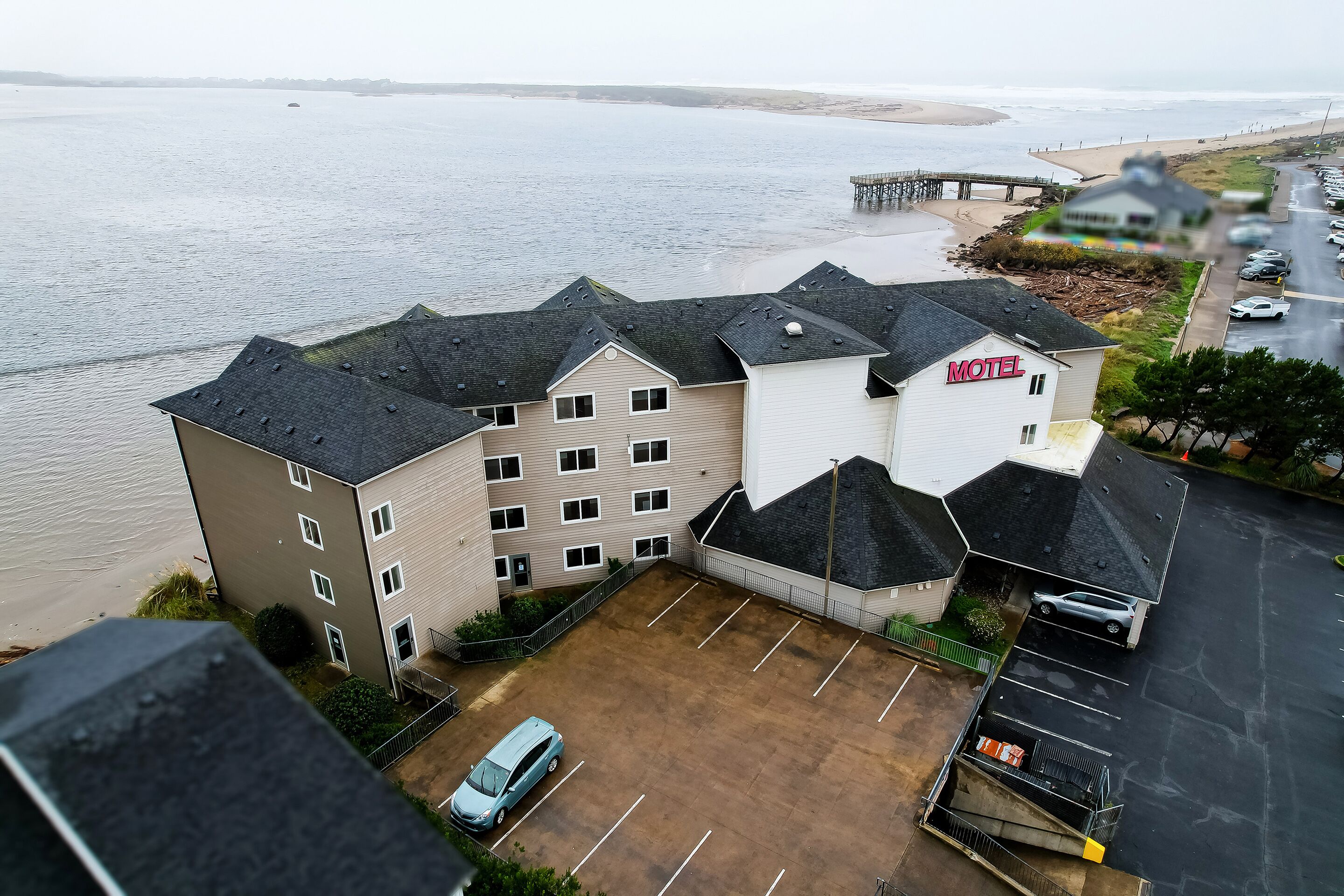 Un motel con parcheggio, vista sulla spiaggia e un molo sullo sfondo.