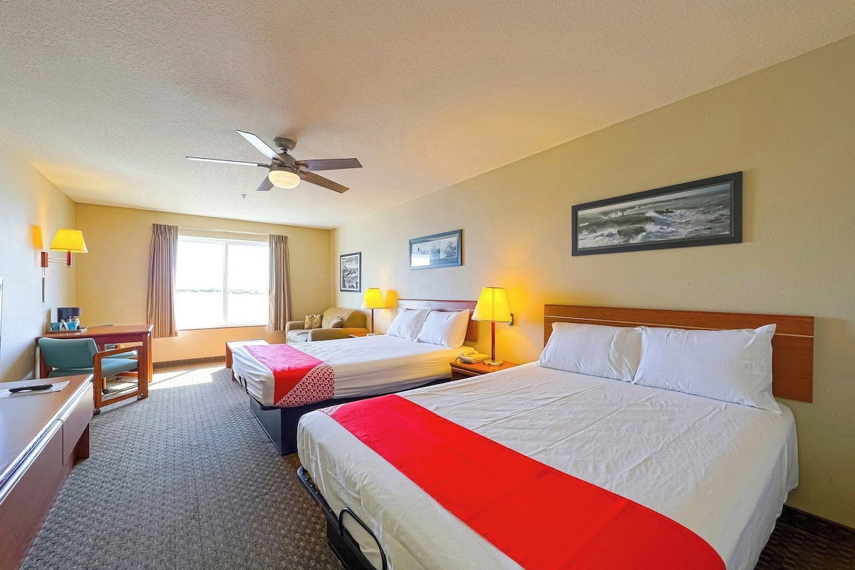 A hotel room with two beds, a desk, a chair, a desk lamp, a telephone, and a ceiling fan.