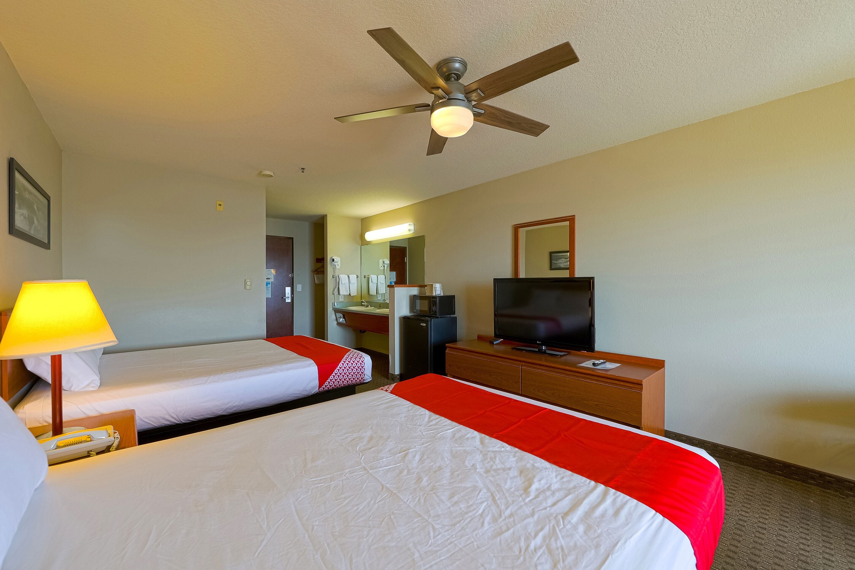 Una habitación de hotel con dos camas, televisión, escritorio y ventilador de techo.