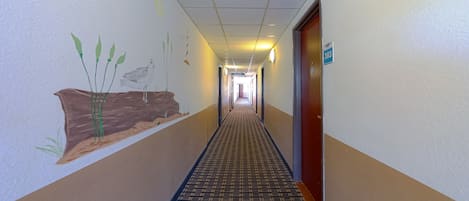 A hotel hallway with a patterned carpet, a mural of plants on the wall, and a door labeled "303".