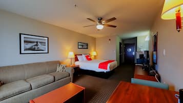 A hotel room with a bed, a sofa, a desk, and a ceiling fan.