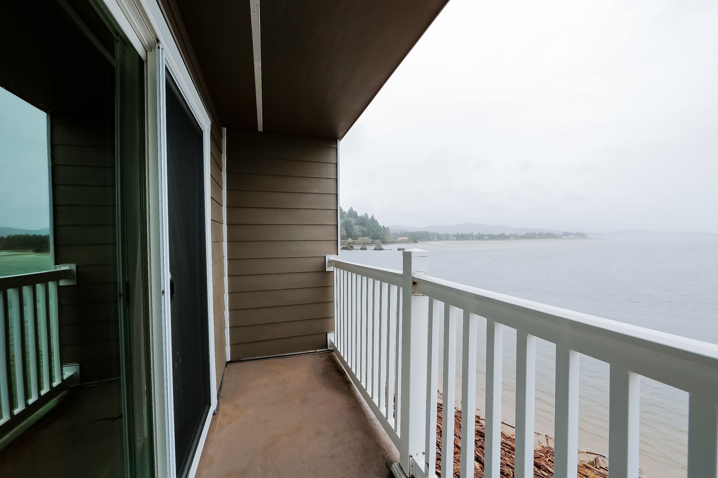 A balcony with a view of a body of water, a white railing, and a door leading to an interior space.