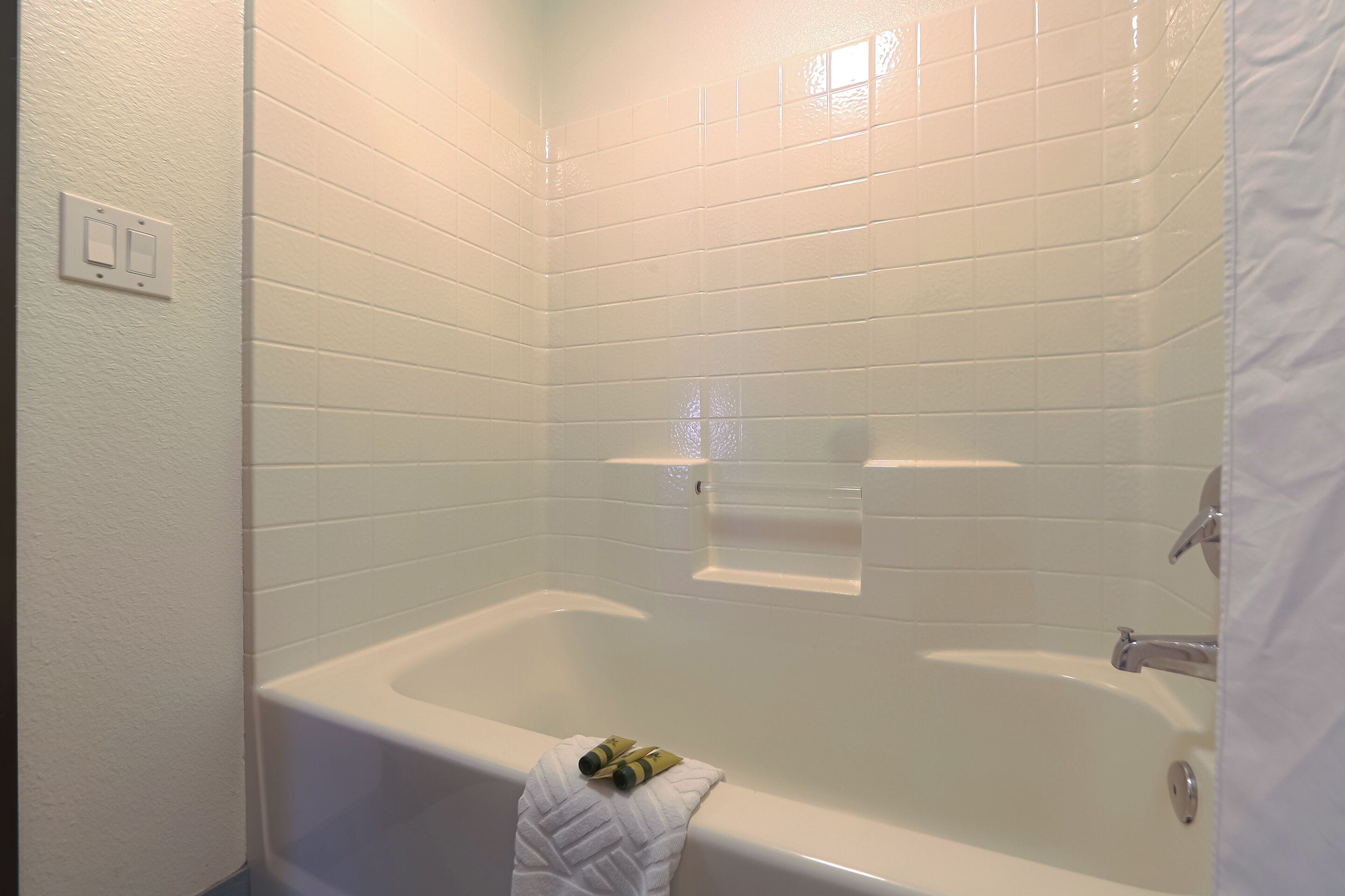 A bathroom with white tiled walls, a bathtub, and a towel rack with a towel.
