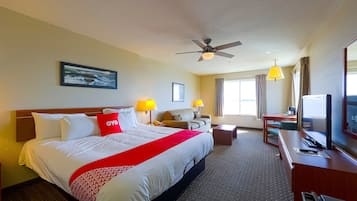 A hotel room with a large bed, a desk, a TV, a ceiling fan, and a window with curtains.