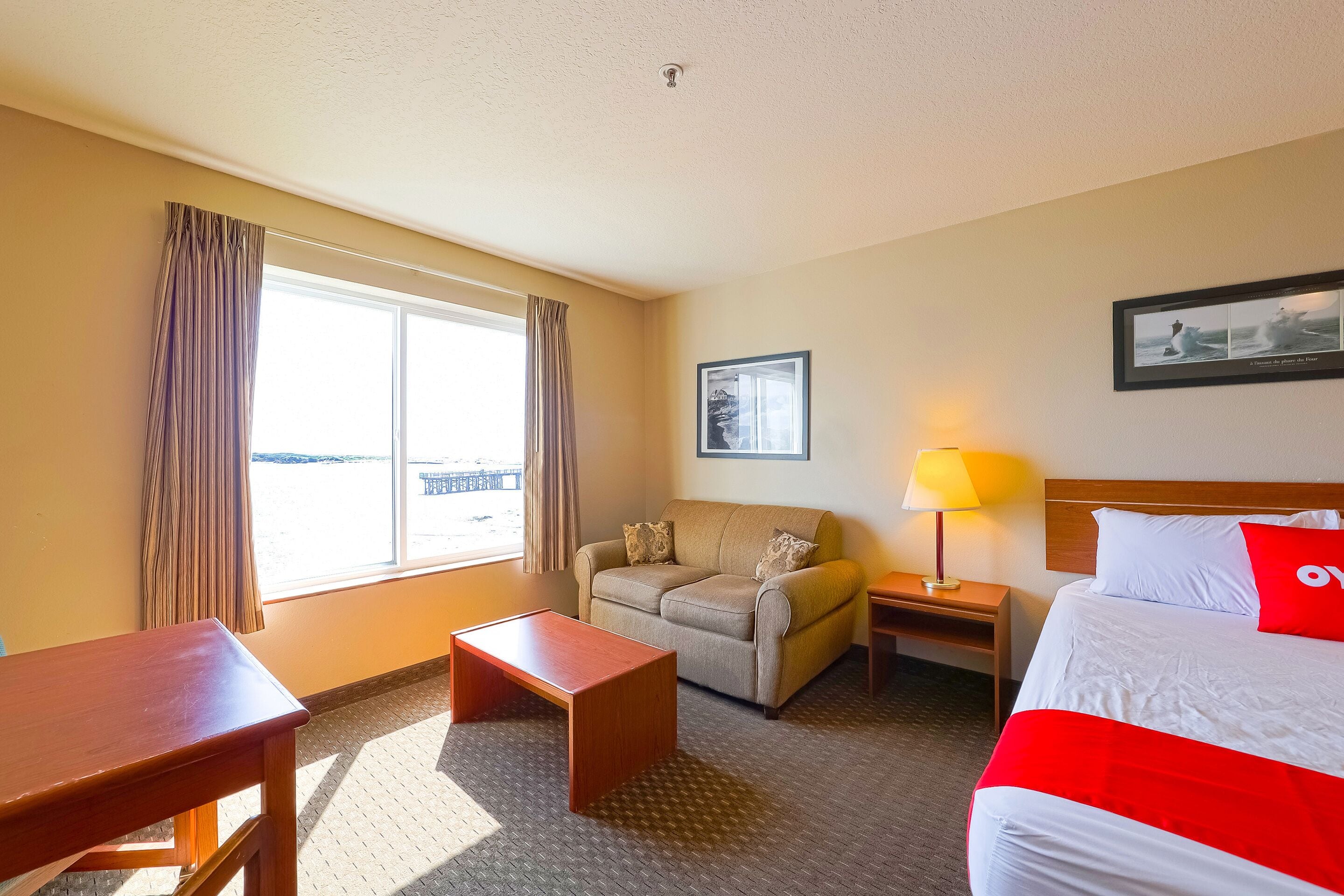 A hotel room with a bed, a sofa, a desk, a lamp, and a window with curtains.