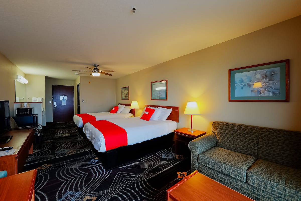 A hotel room with a bed, two bedside tables, a sofa, a desk, a chair, a television, and a ceiling fan.