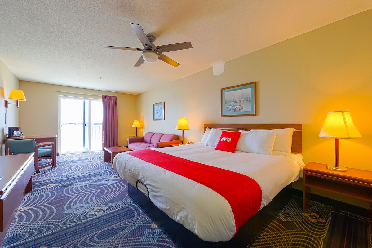 A hotel room with a bed, desk, chair, lamps, and a ceiling fan.