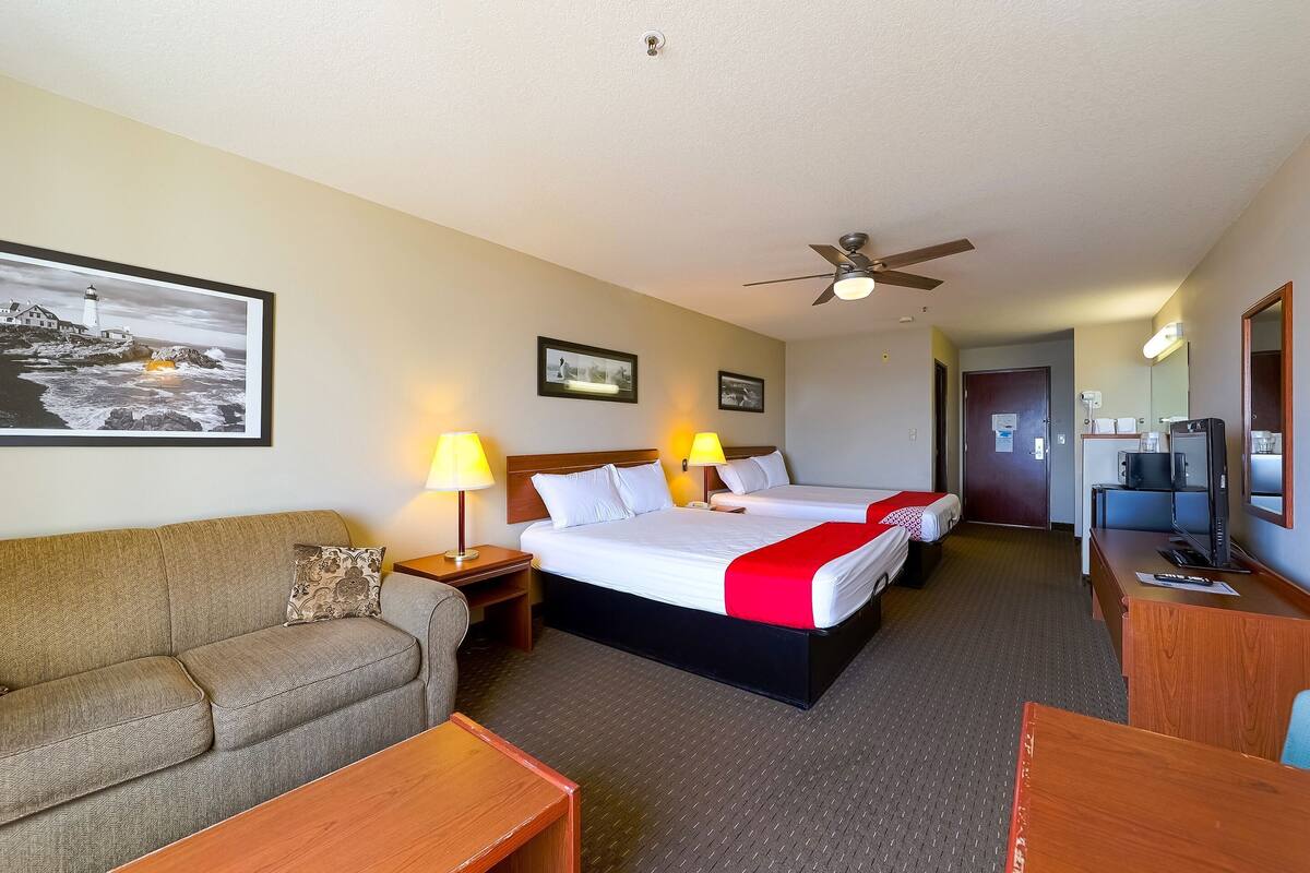 A hotel room with a bed, two bedside tables with lamps, a sofa, a desk, a television, and a ceiling fan.
