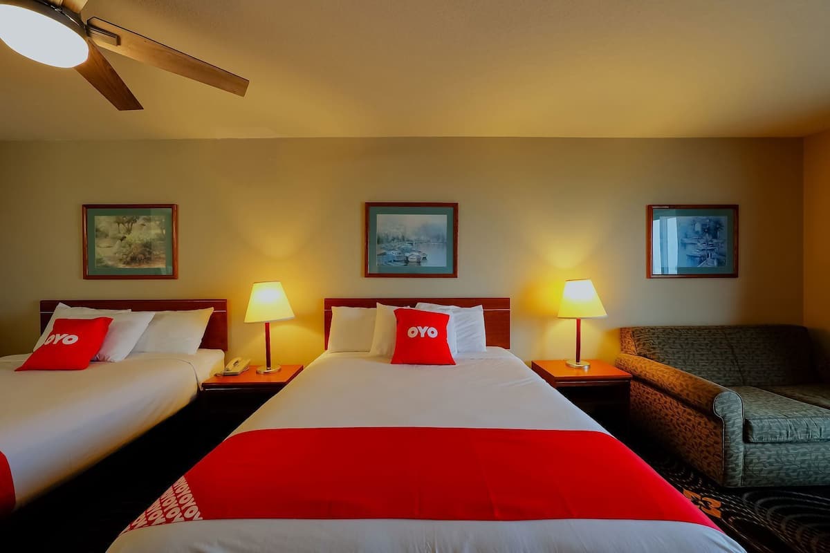 A hotel room with two beds, a ceiling fan, and three framed pictures on the wall.