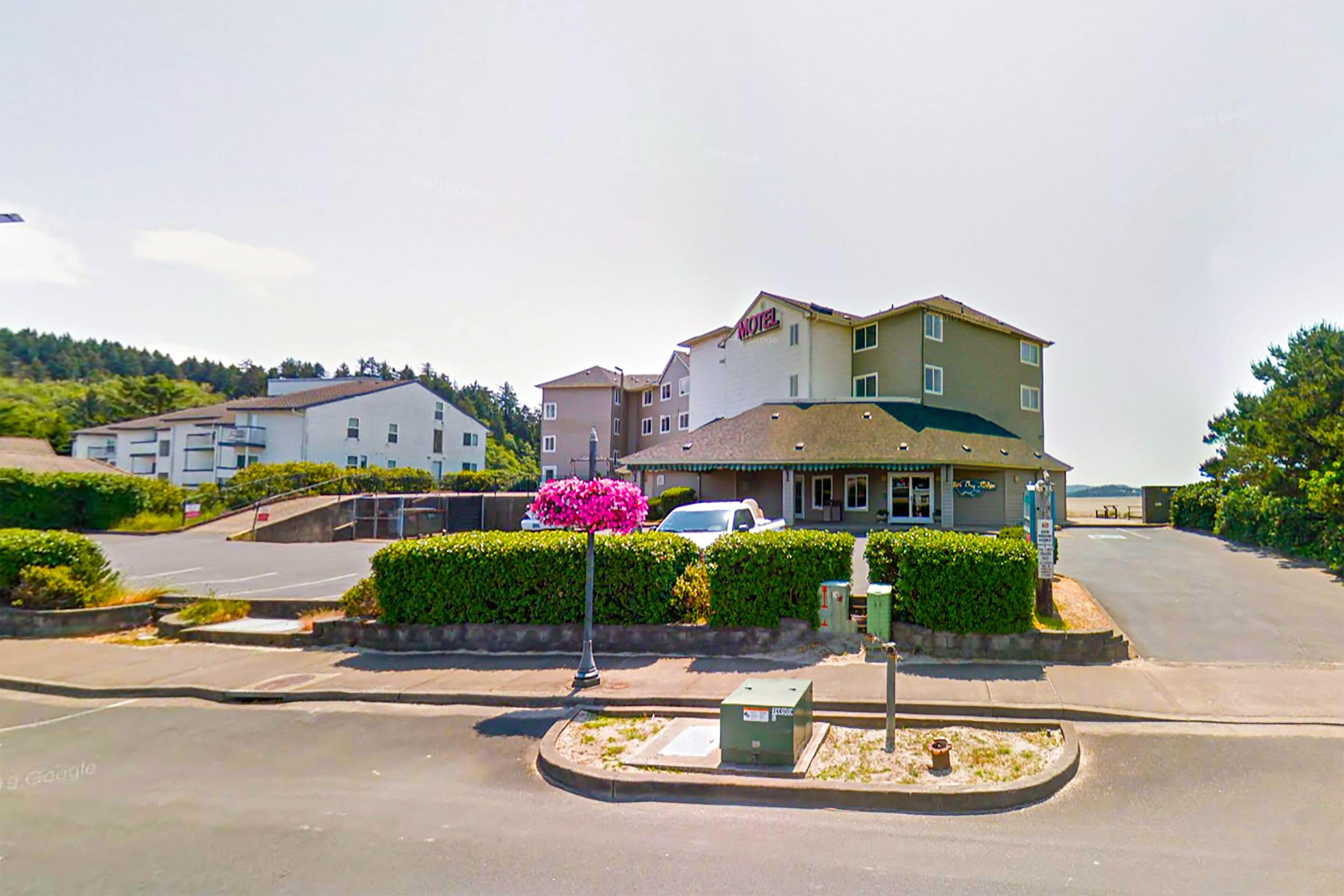 A hotel with a prominent 'HOTEL' sign, a parking lot, and a landscaped area with a flower bush.