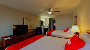 A hotel room with two beds, a TV, a desk, a ceiling fan, and a bathroom visible in the background.