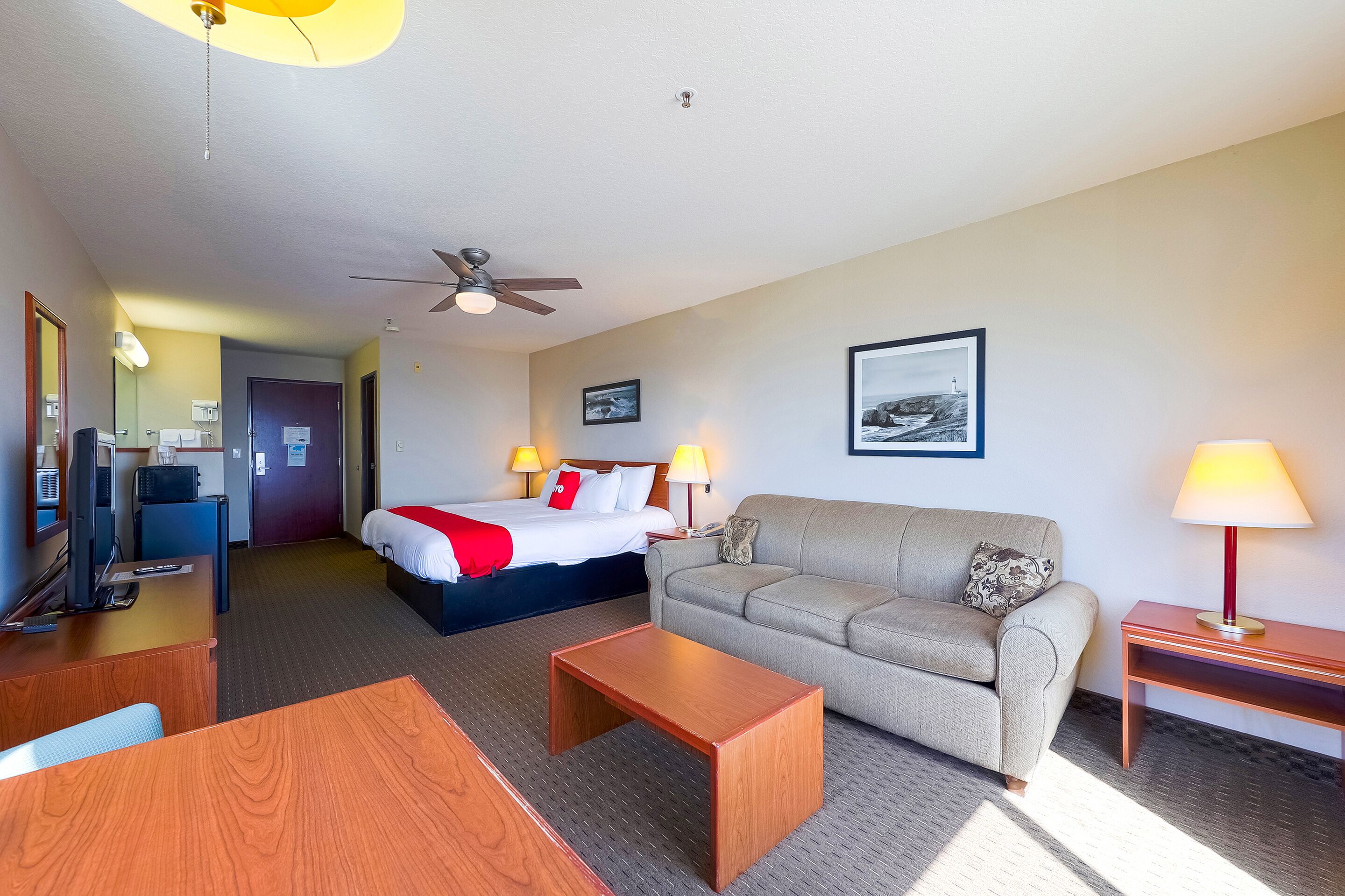 Habitación de hotel con cama, sofá, escritorio, mesa de centro y ventilador de techo.