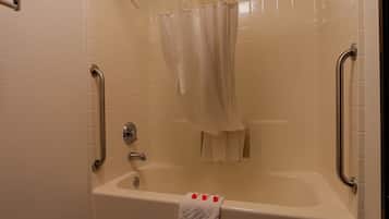 A bathroom with a bathtub, a shower curtain, and grab bars.