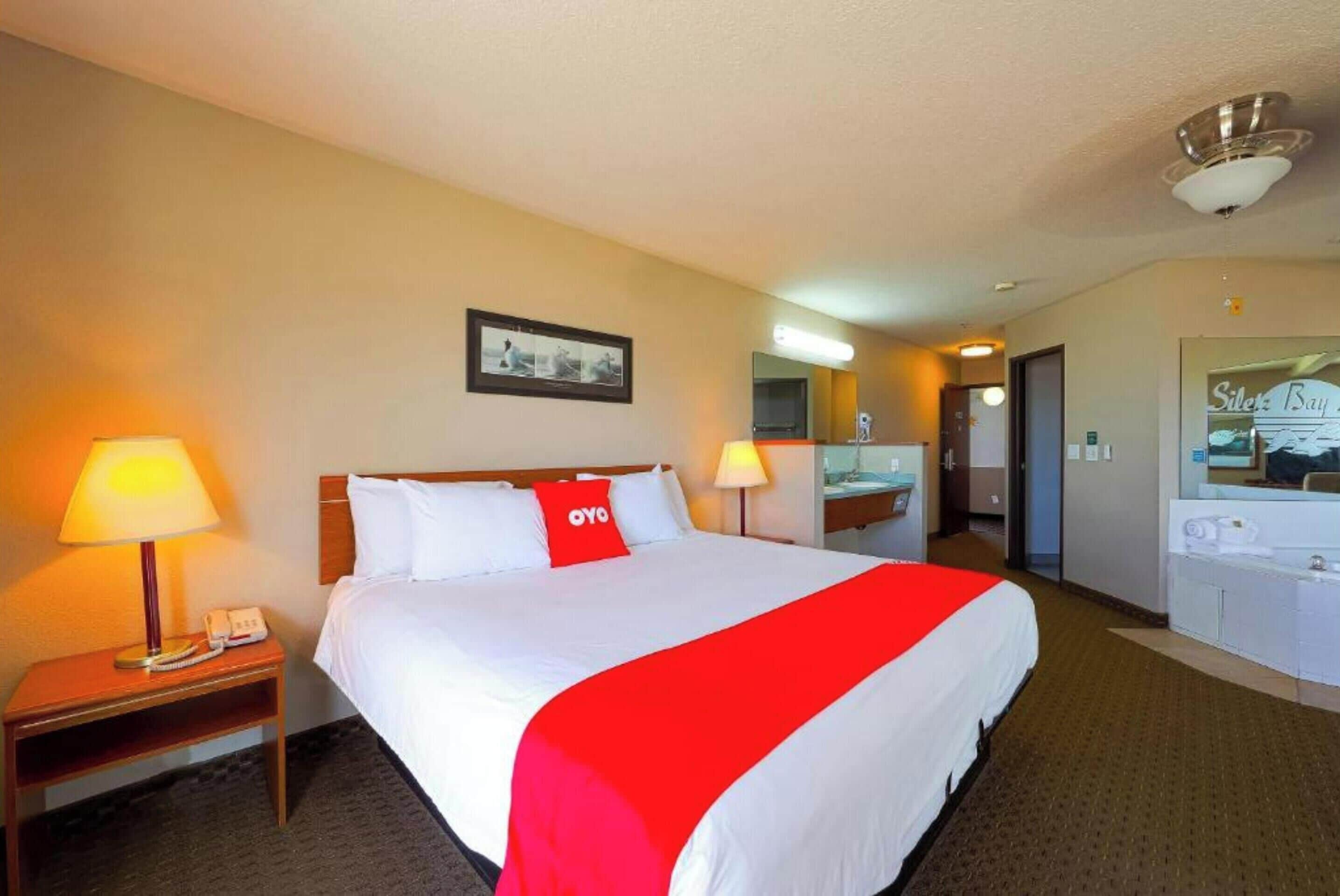 A hotel room with a large bed, two bedside lamps, a telephone, a mirror, and a bathroom visible through an open door.