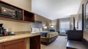 A hotel room with a kitchenette, a bed with a blue blanket, a desk, and a large window with curtains. - Comfort Inn & Suites North Little Rock McCain Mall (North Little Rock)