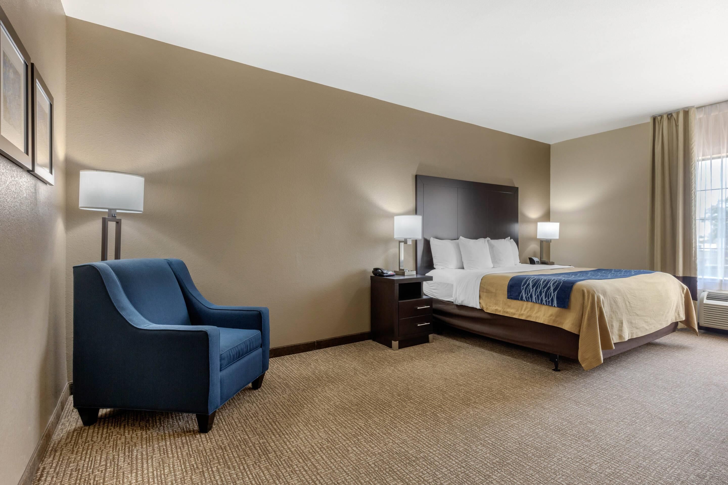 A hotel room with a bed, a chair, a nightstand, and a lamp.