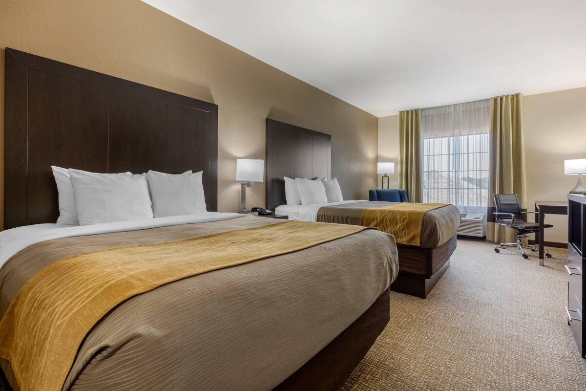 Een hotelkamer met twee bedden, een bureau, een stoel en een groot raam met gordijnen.