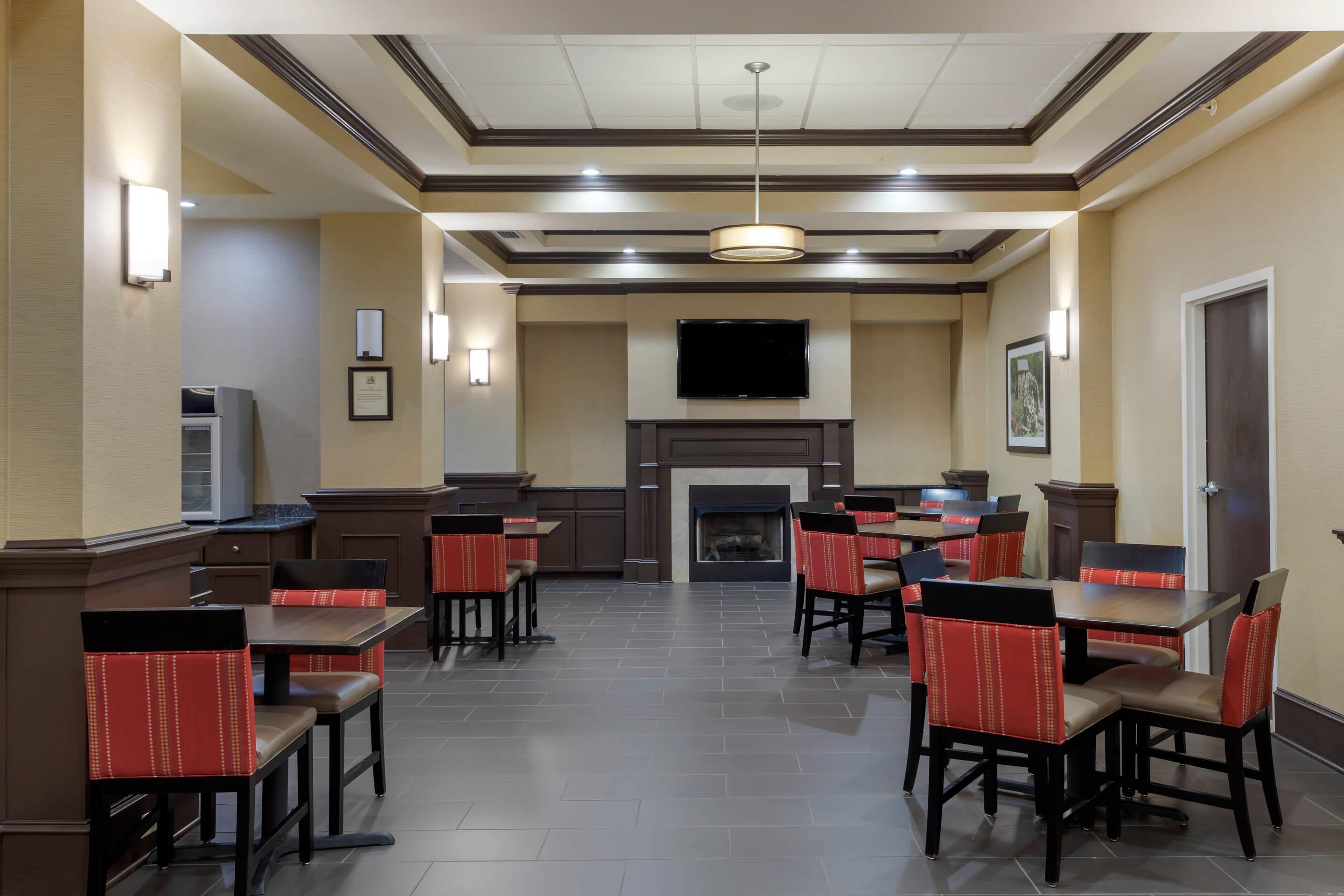 A hotel dining area with multiple tables and chairs, a fireplace, and a television mounted on the wall.