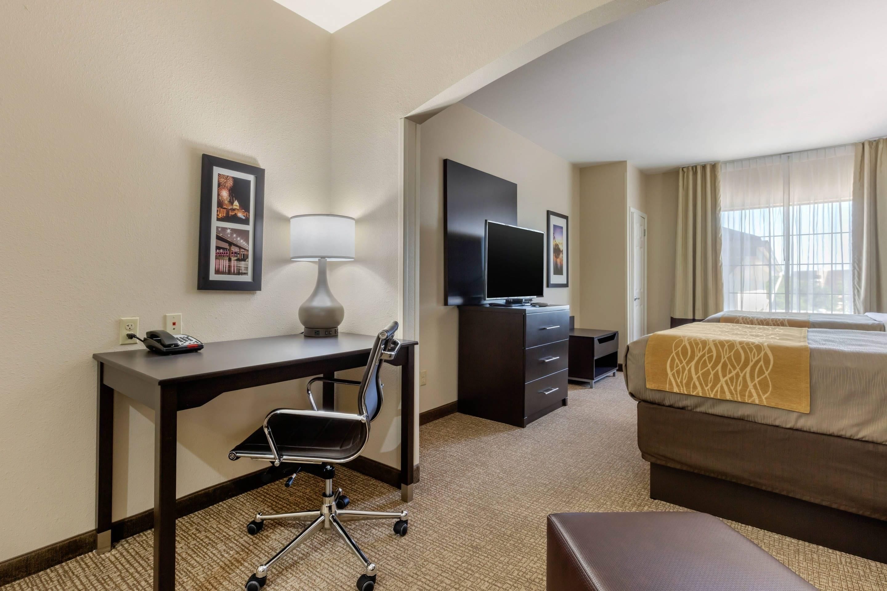 A hotel room with a desk, chair, television, bed, and a window with curtains.