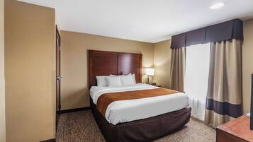 Habitación de hotel con una cama grande, cabecera de madera, lámpara de noche y vistas al exterior a través de cortinas.