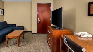 Una habitación de hotel con un escritorio de madera, televisor, sofá y cómoda de madera.