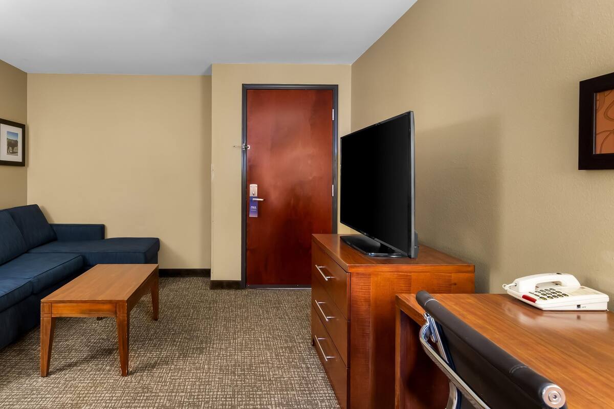 A hotel room with a wooden desk, a television, a sofa, and a wooden dresser.