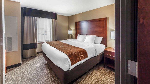 Habitación de hotel con una cama grande, cabecero de madera, mesita de noche con lámpara y ventana con cortinas.