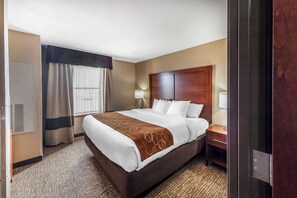 Habitación de hotel con una cama grande, cabecero de madera, mesita de noche con lámpara y ventana con cortinas.