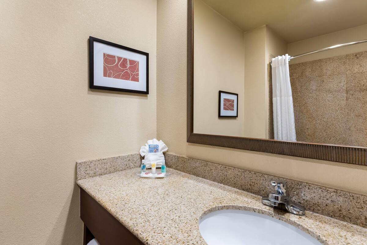 A bathroom with a granite countertop, a sink, a mirror, and framed artwork on the wall.