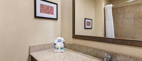 A bathroom with a granite countertop, a sink, a mirror, and framed artwork on the wall.