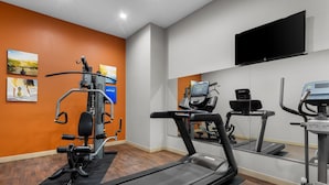 Un gimnasio moderno con equipo de cardio, un espejo grande y un televisor montado.