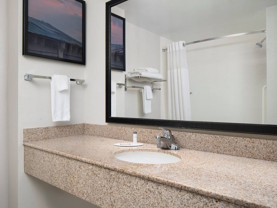 Un baño con encimera de granito, un lavabo, un espejo y una cortina de ducha.
