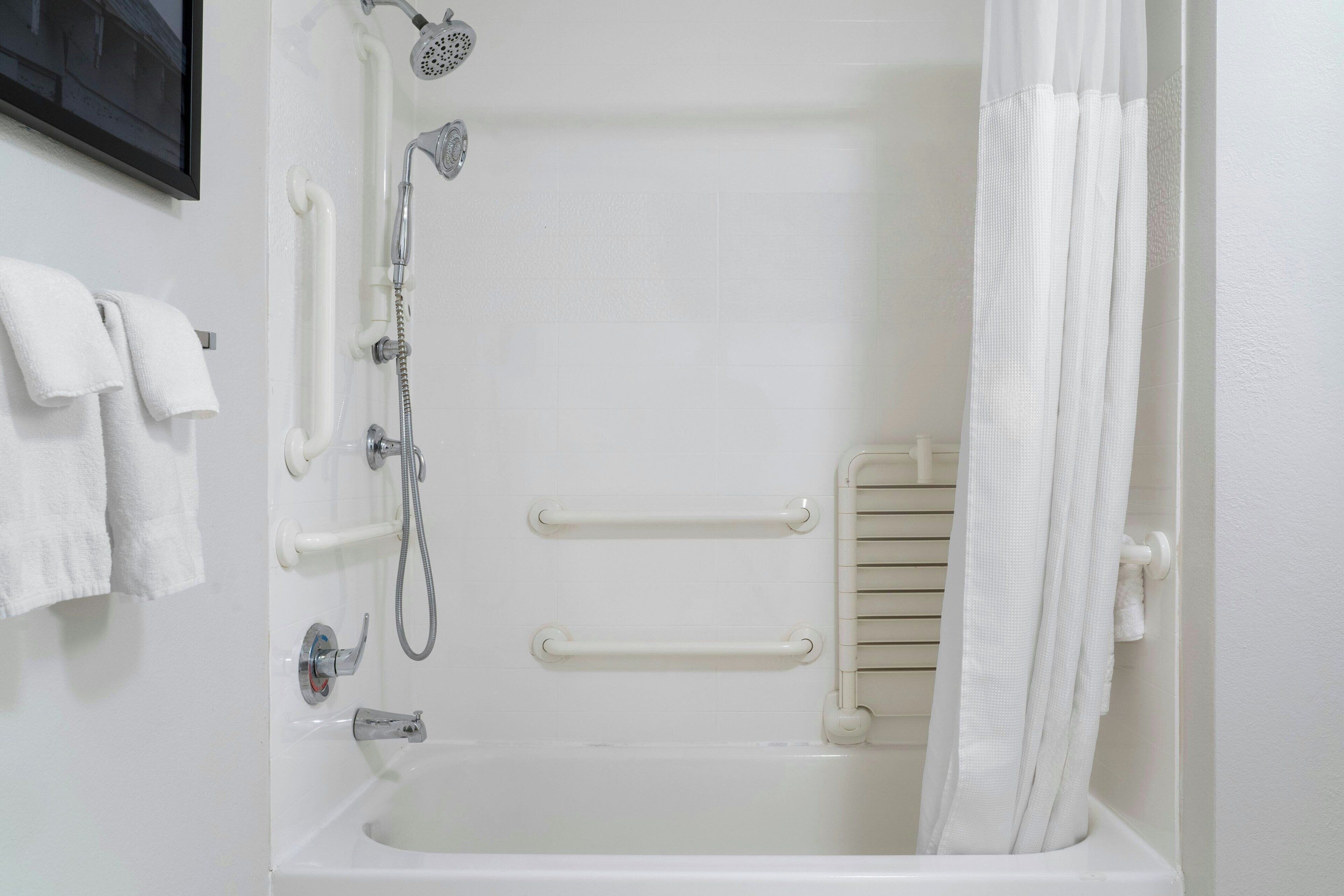 A white bathtub with a showerhead, grab bars, and a towel rack.