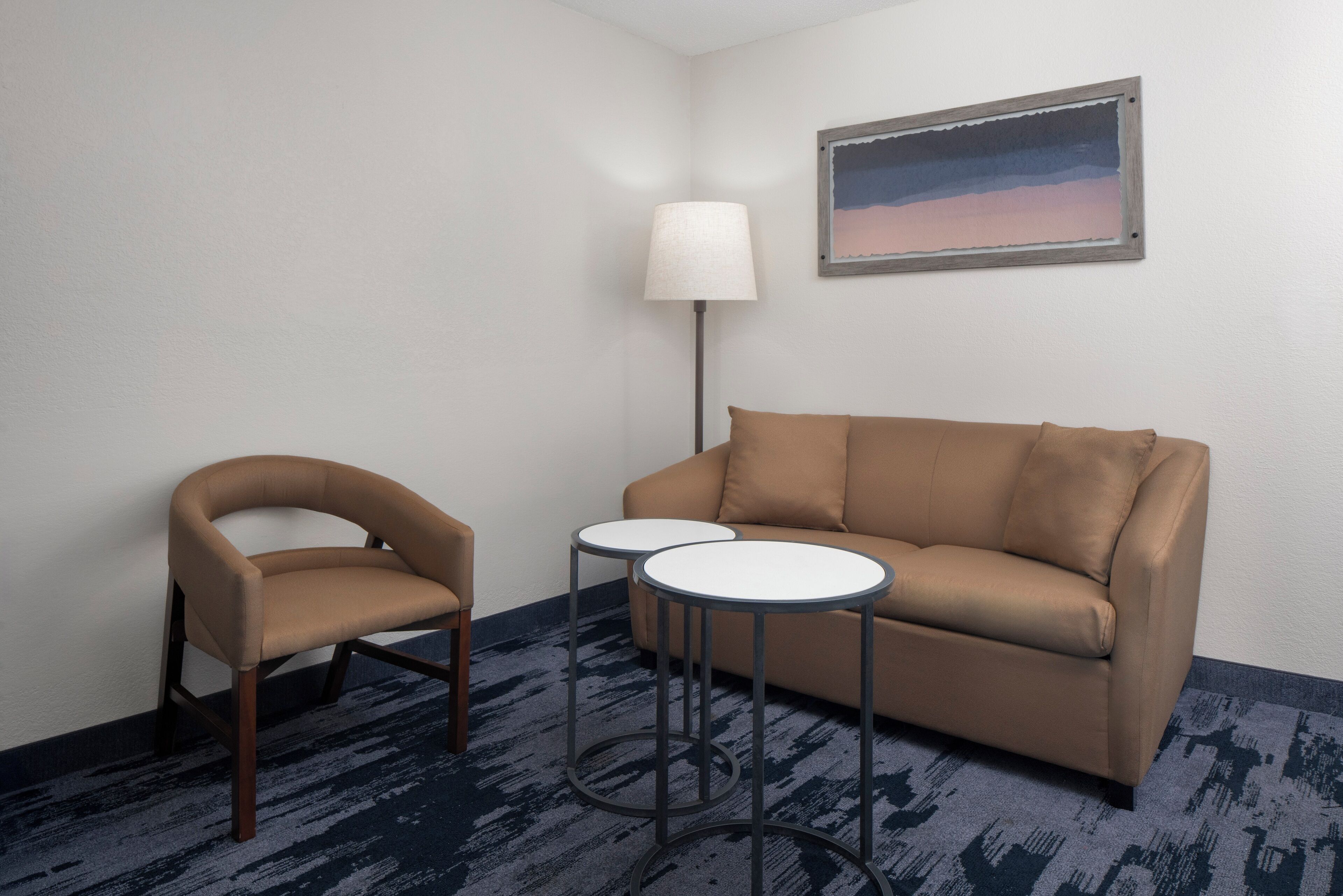Una habitación con un sofá marrón, un sillón marrón y dos mesitas redondas.