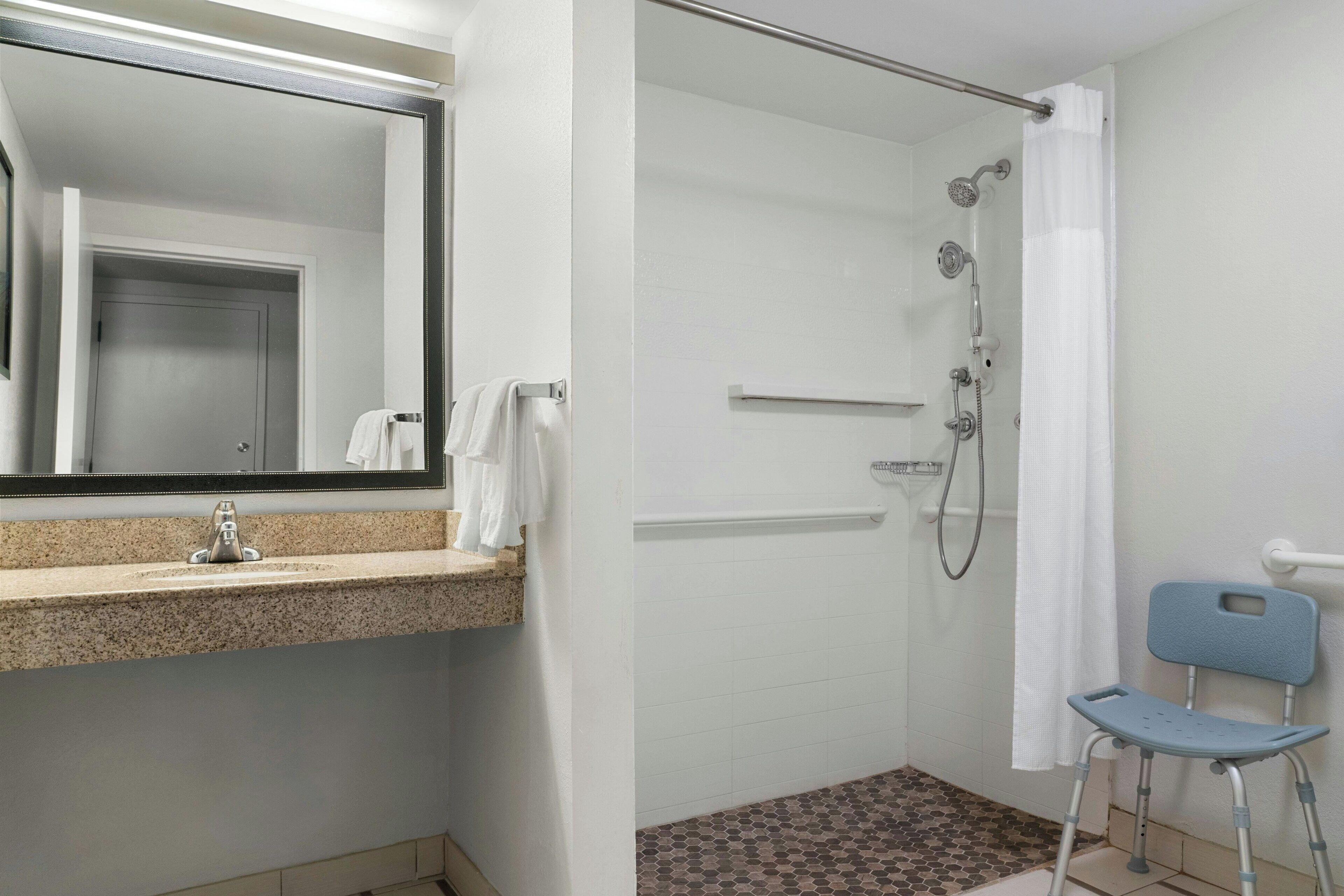 Un baño con lavamanos, espejo, ducha y una silla de ruedas.